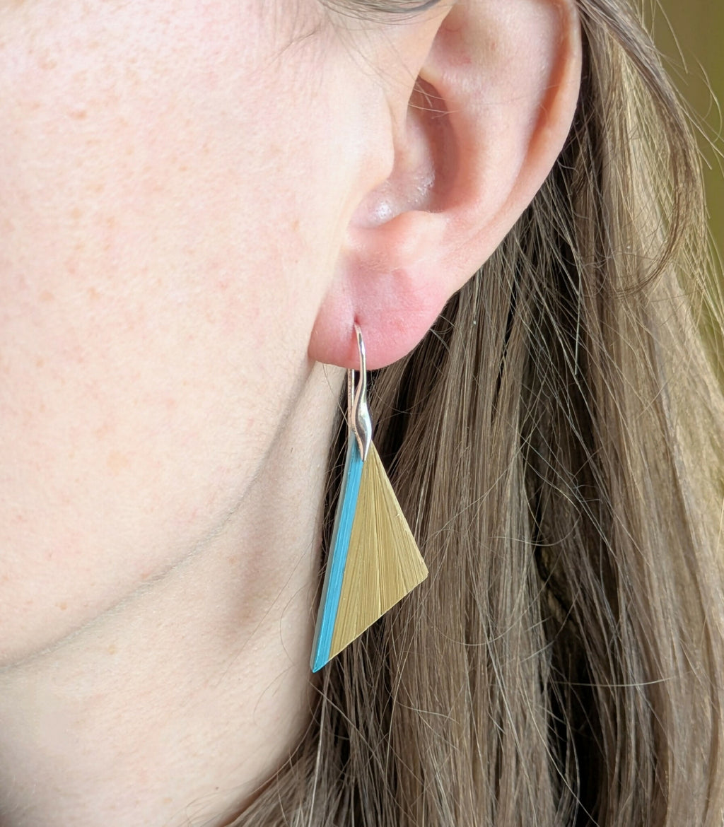 Boucles d’oreilles triangulaires paille dorée et turquoise, sur crochets argent, portées.