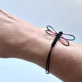 Bracelet noir en cordon tressé, libellule peinte rose et rouge près du poignet.