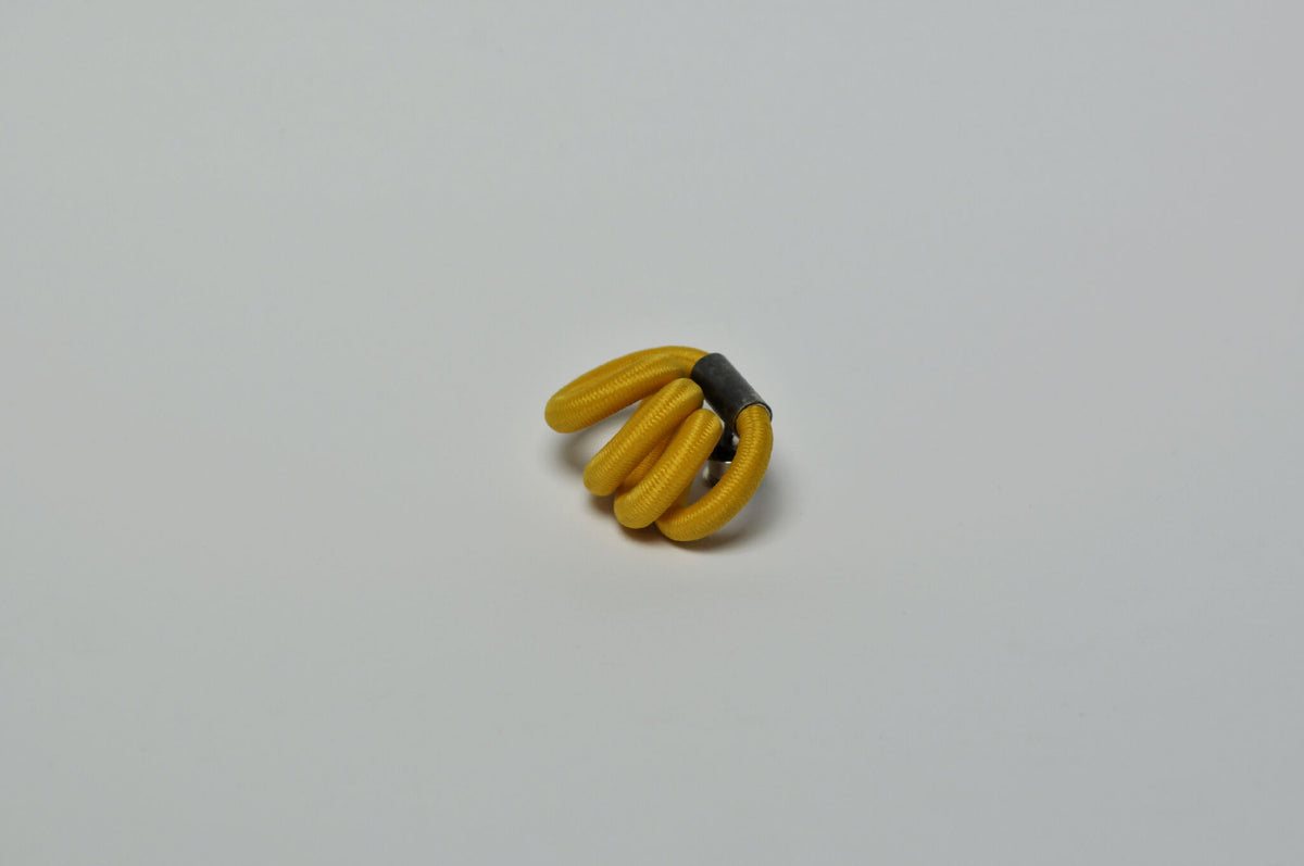 Broche entrelacée jaune, fermoir noir visible, vue rapprochée.
