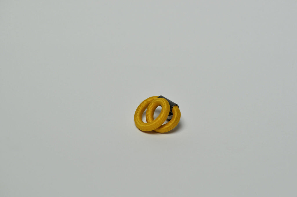 Broche entrelacée jaune, fermoir noir partiellement visible.