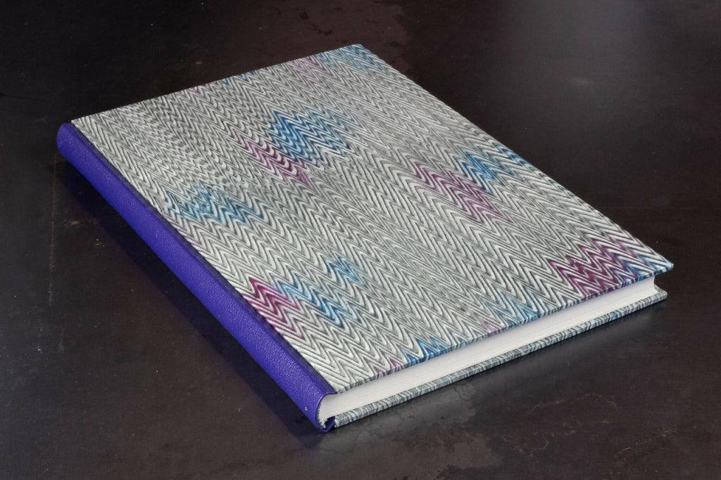 Carnet à couverture rigide grise à motif, dos en cuir violet.