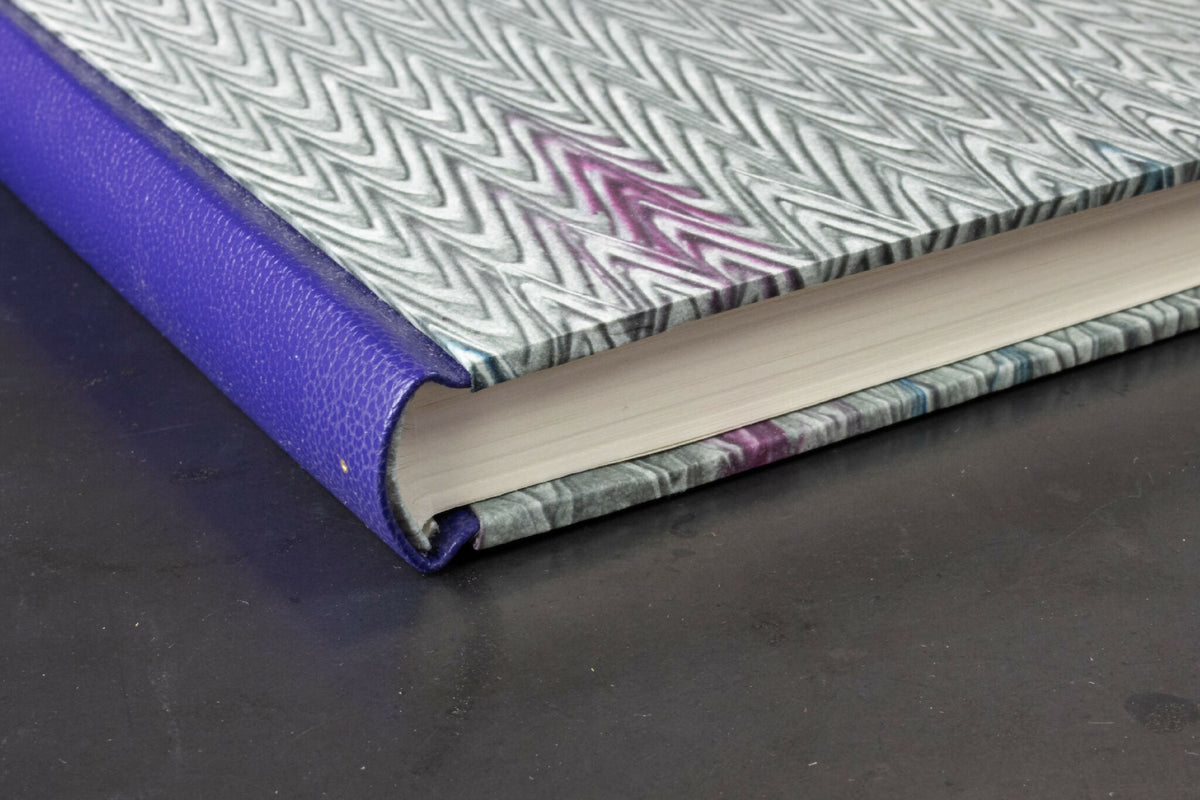 Carnet à dos en cuir violet et tranches crème visibles, couverture motif zigzag.