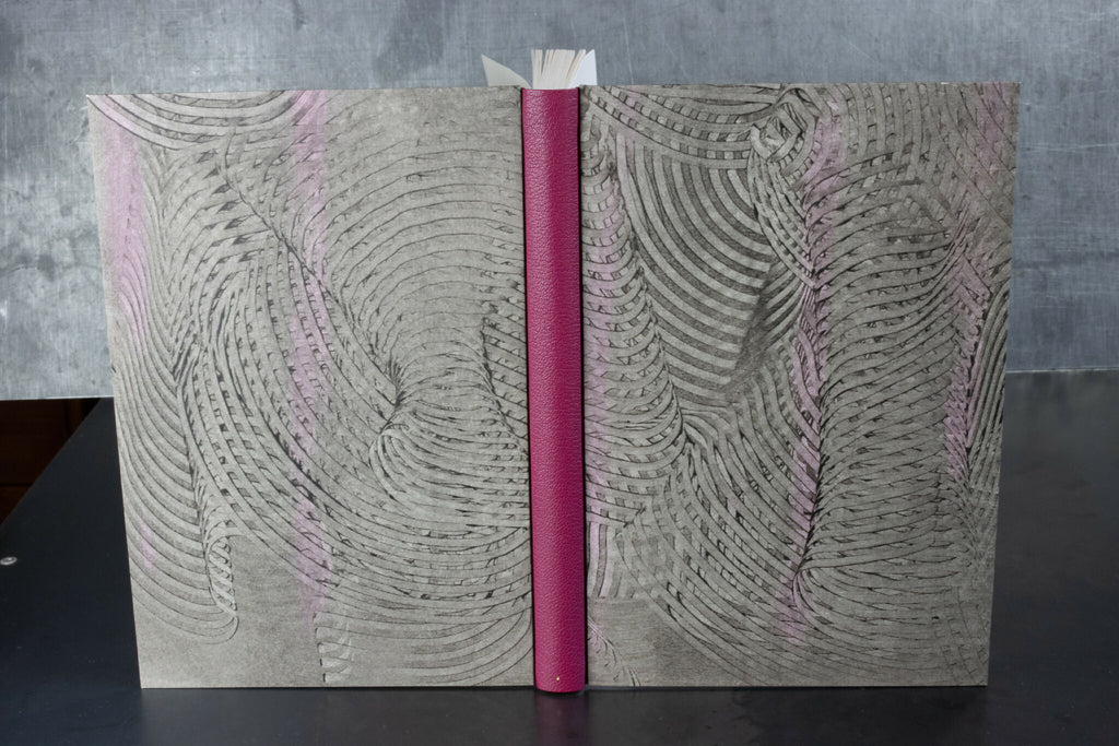 Cahier à couverture cuir gris, motifs ondulés, dos fuchsia et reliure centrale.
