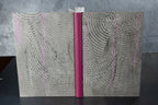 Cahier à couverture cuir gris, motifs ondulés, dos fuchsia et reliure centrale.
