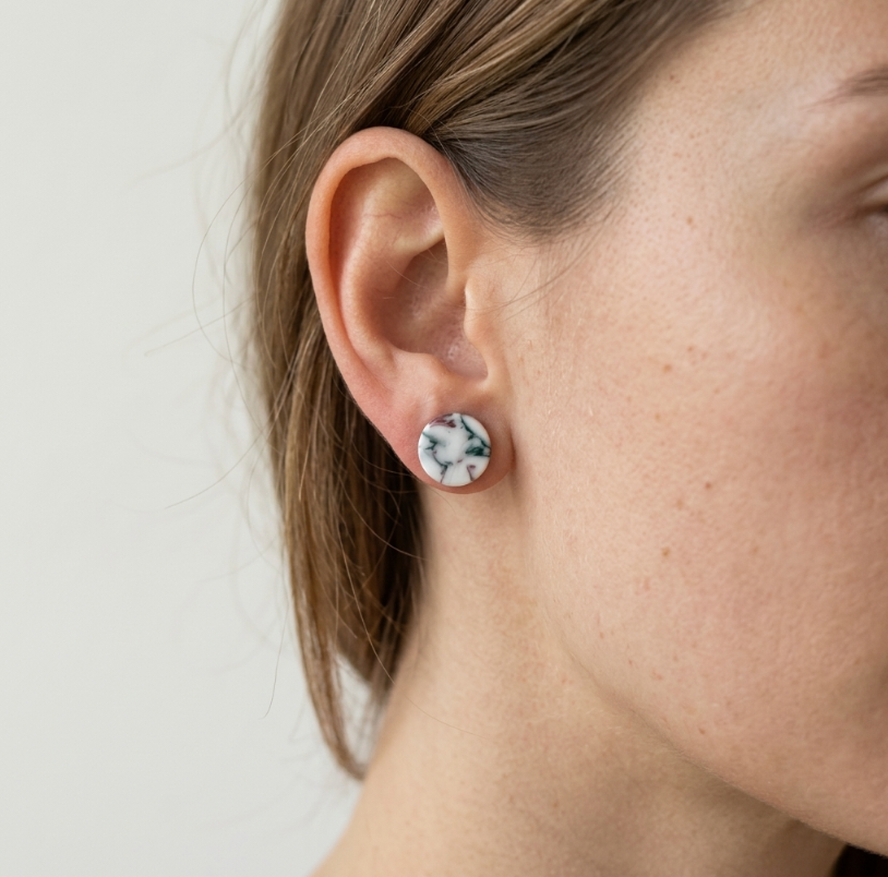 Clous d’oreille ronds en porcelaine, motif marbré blanc, bleu et rose, sur l’oreille.