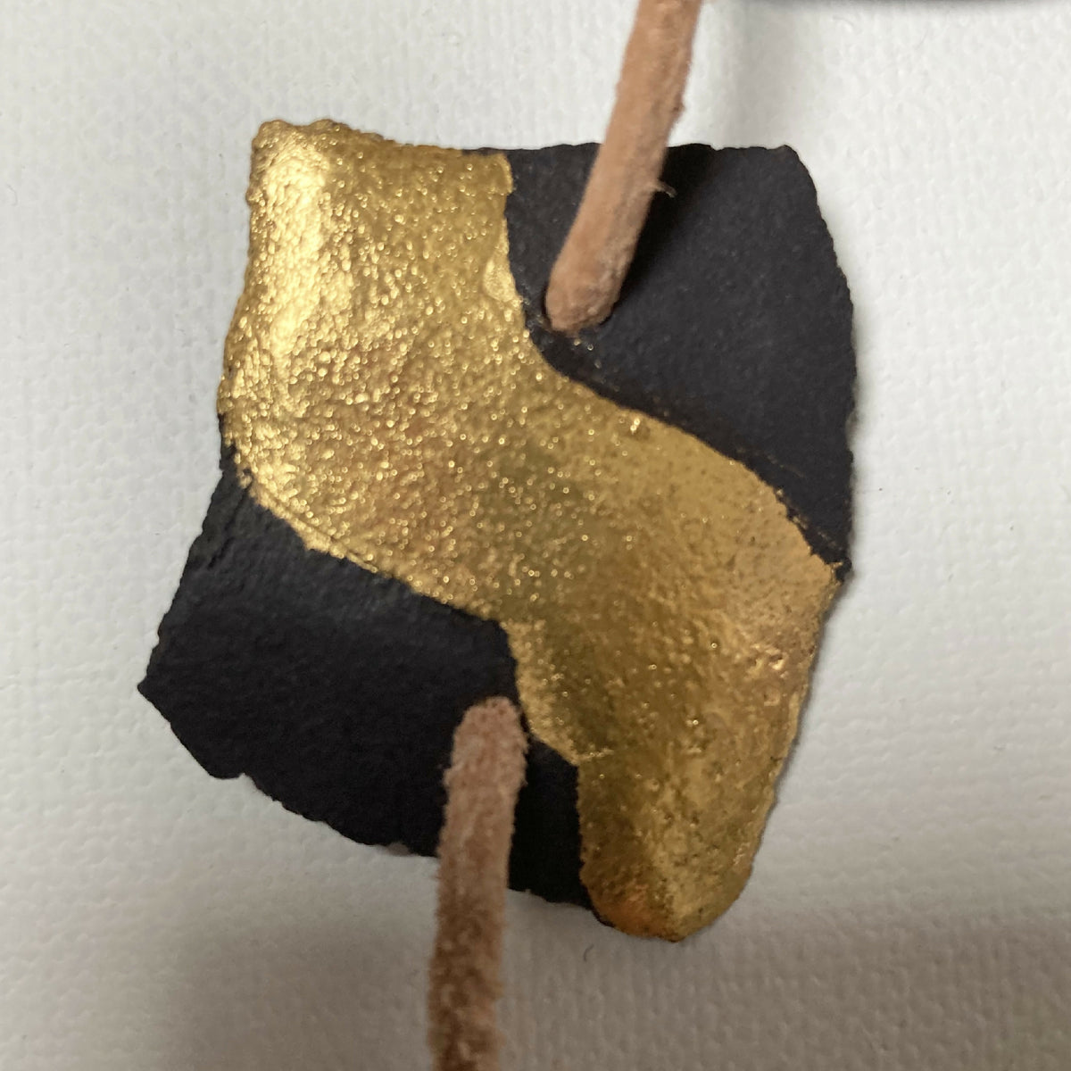 Pendentif doré et noir, forme abstraite, monté sur cordon beige