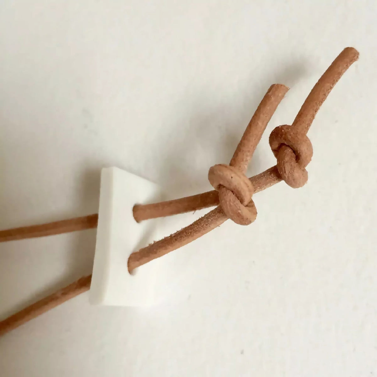 Collier : nœud en cordon beige et petite pièce dorée de fixation