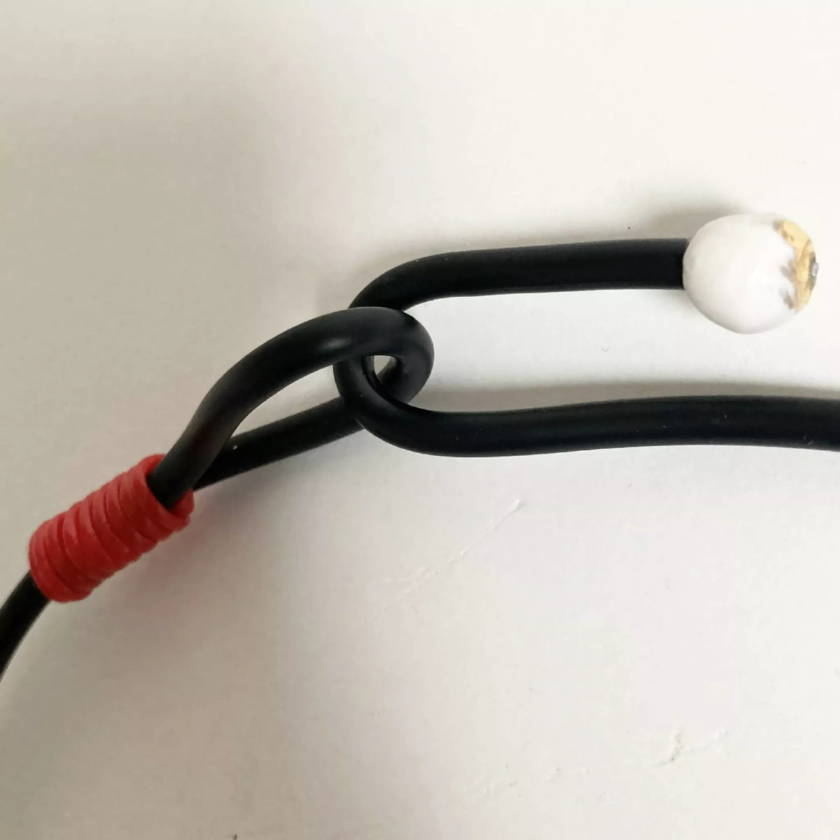 Fermoir du collier : cordon noir avec perle blanche et embout rouge