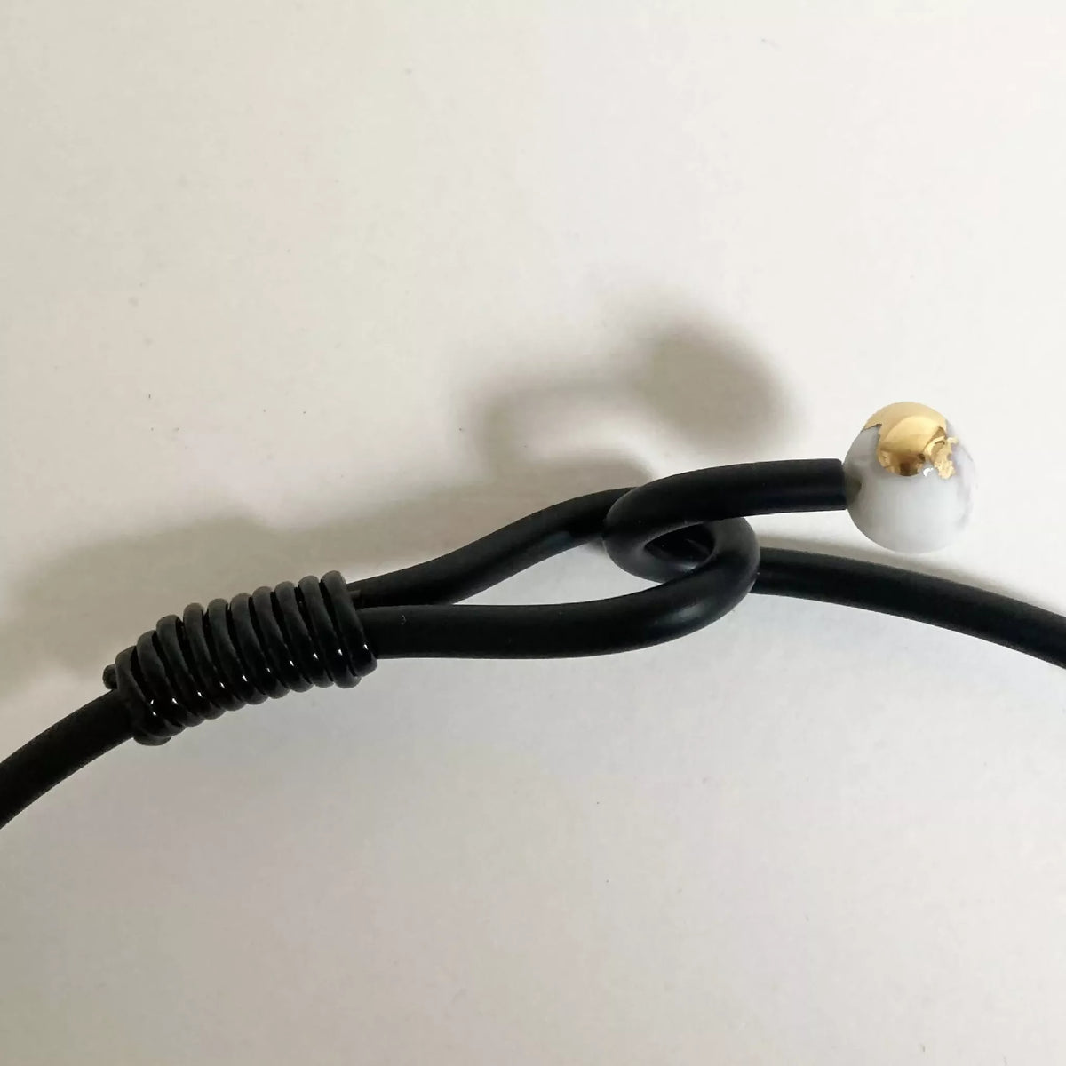 Fermoir du collier : cordon noir et attache ronde beige, détail du bracelet