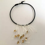 Collier à cordon noir avec franges blanches et plusieurs breloques dorées, vue de face