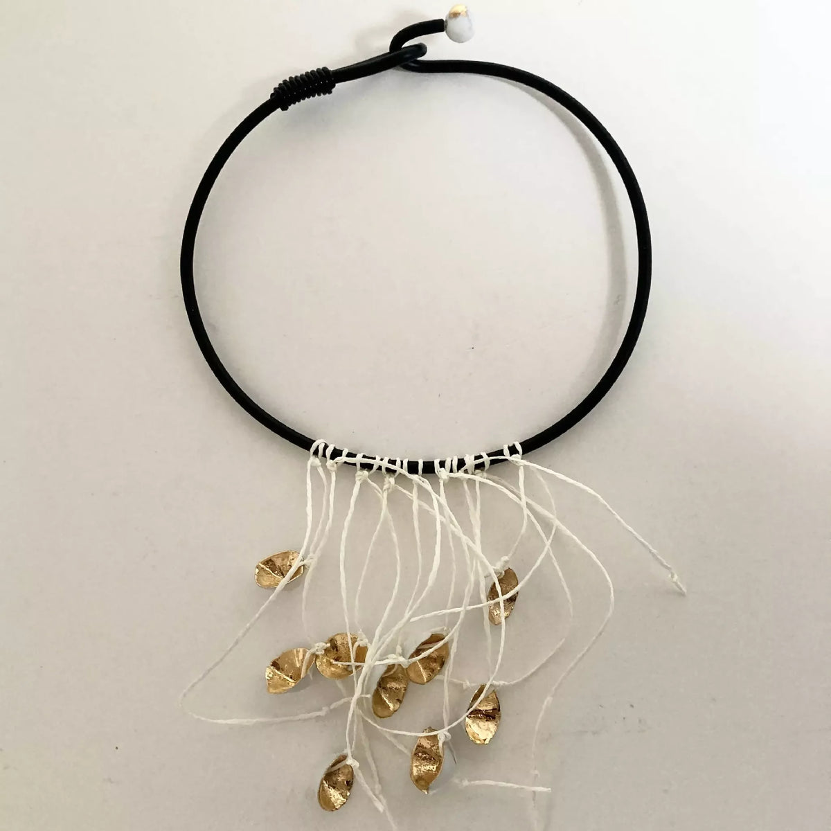 Collier à cordon noir avec franges blanches et plusieurs breloques dorées, vue de face