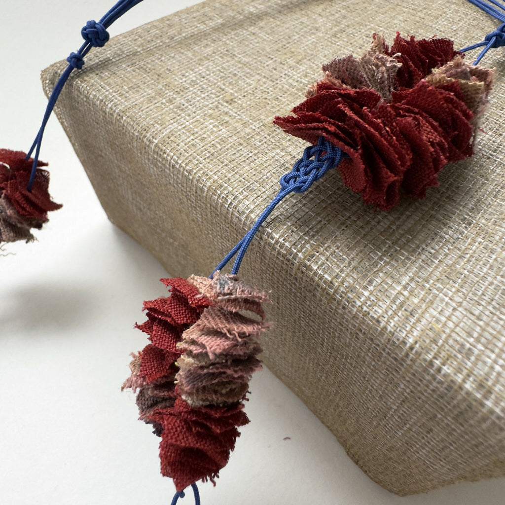 Détail du collier : fleurs en tissu bordeaux et gris sur cordon bleu