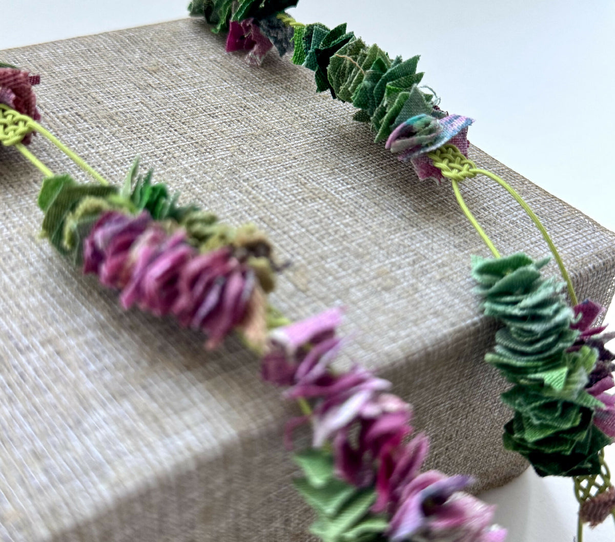 Collier vert et violet, gros plan sur perles tressées et rosettes en tissu