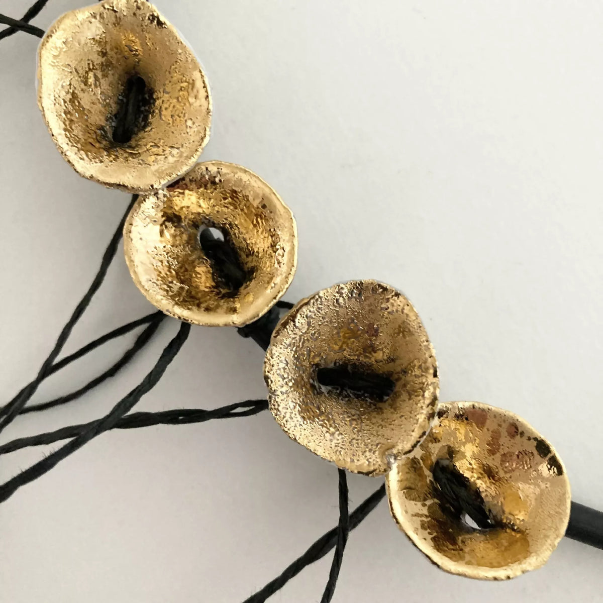 Collier en gros plan : disques dorés irréguliers et cordons noirs noués