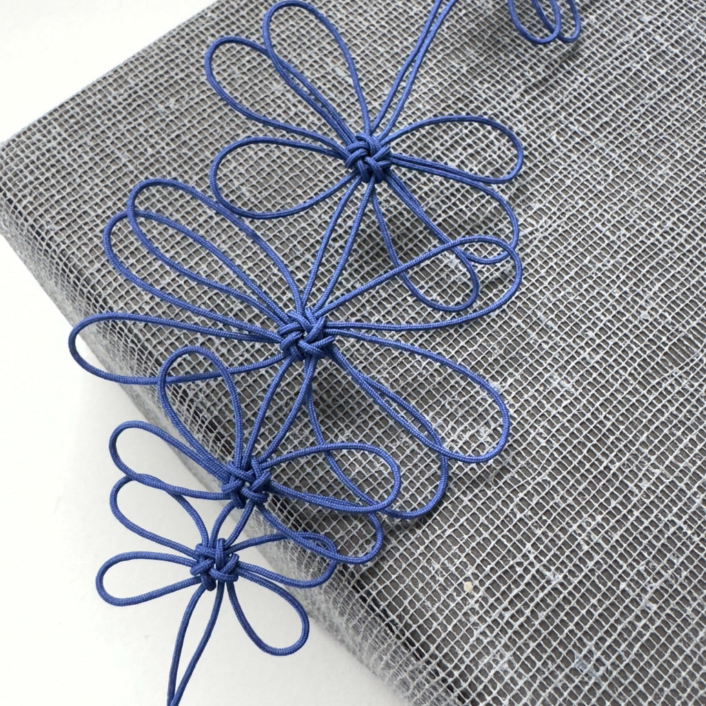 Collier de fleurs de prunier bleu : gros plan sur fleurs en fil et pétales bouclés.