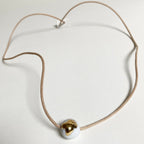 Collier en porcelaine à pendentif rond doré, cordon marron et base claire.