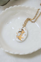 Collier en porcelaine : médaillon ovale blanc avec hirondelles dorées, chaîne dorée