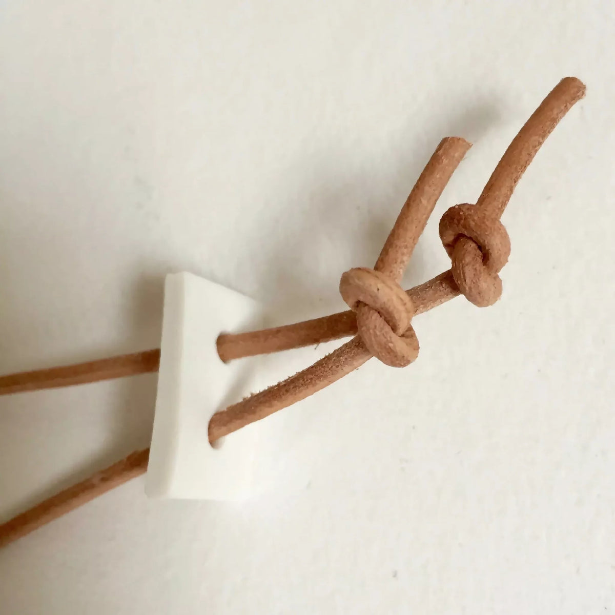 Attache du collier : cordon brun noué sur support blanc en forme de crochet