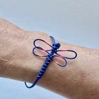 Bracelet fin bleu avec motif de libellule rose, nœuds décoratifs et cordon réglable.