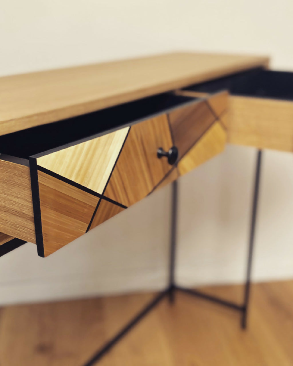 Détail de console en chêne : tiroir à losanges et bouton noir, structure noire