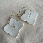 Boucles d’oreilles créoles avec fleurs en porcelaine blanche et montures dorées.