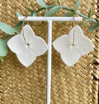 Paire de créoles fleurs en porcelaine blanche, monture dorée sur support blanc.