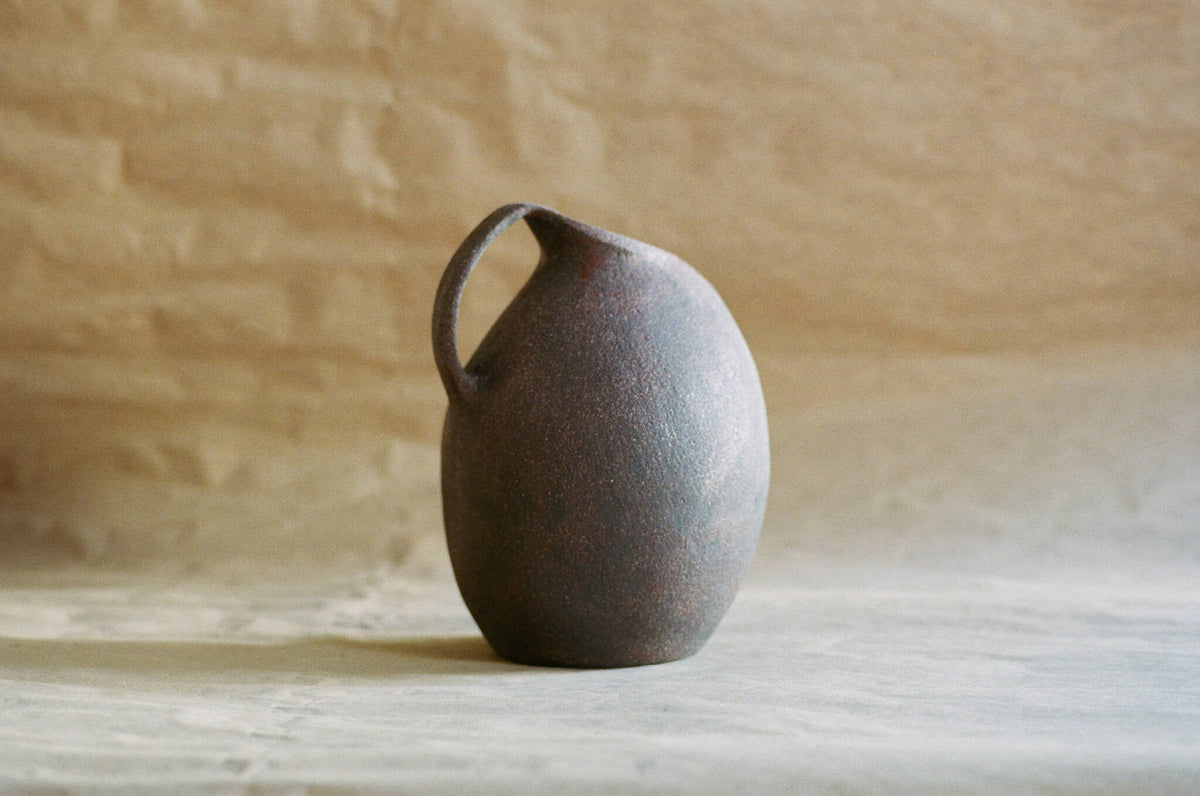Cruche en céramique sombre, anse courbée, forme arrondie