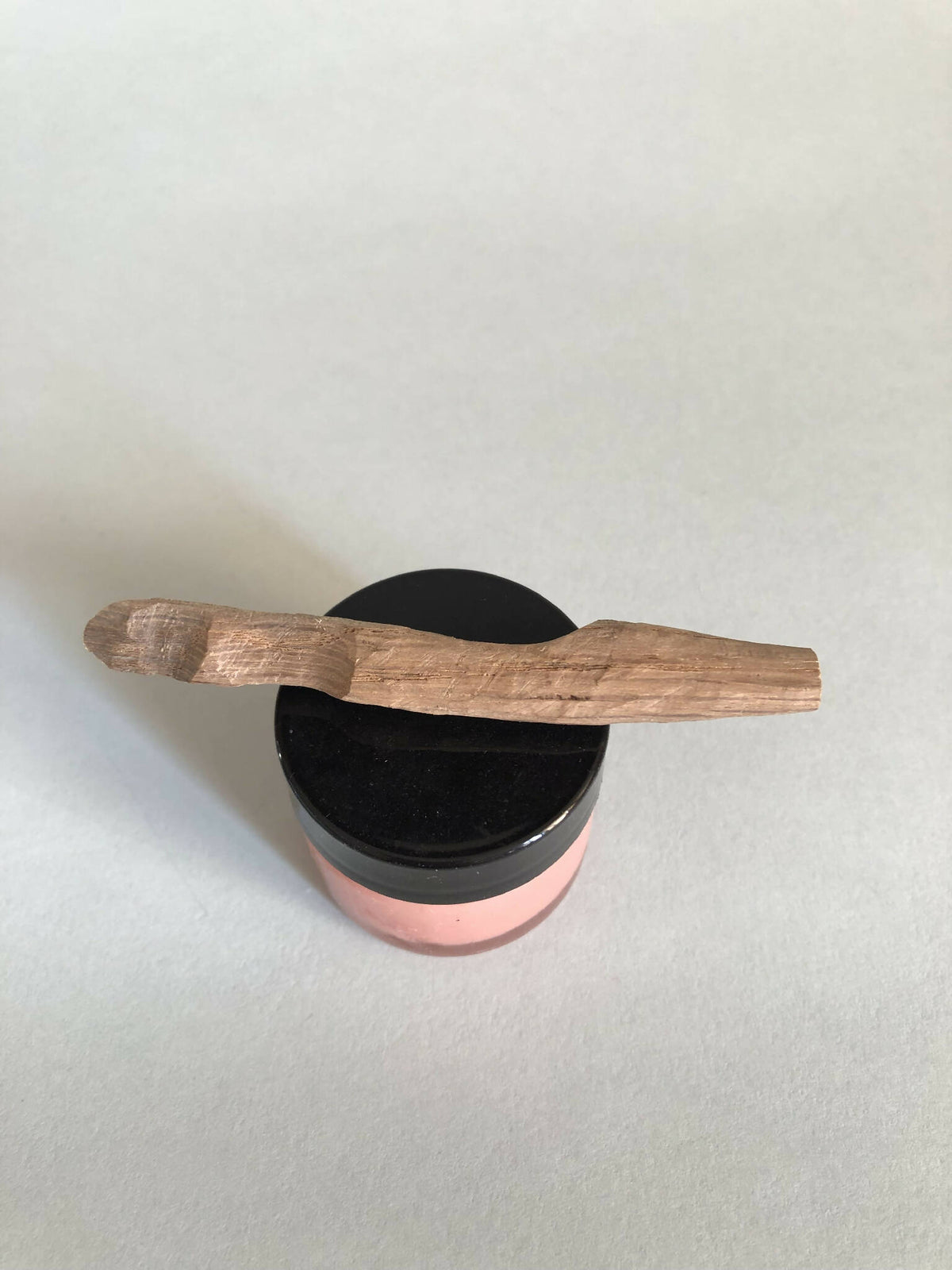 Cuillère à cosmétiques en bois, manche horizontal, posée sur un pot à couvercle noir.