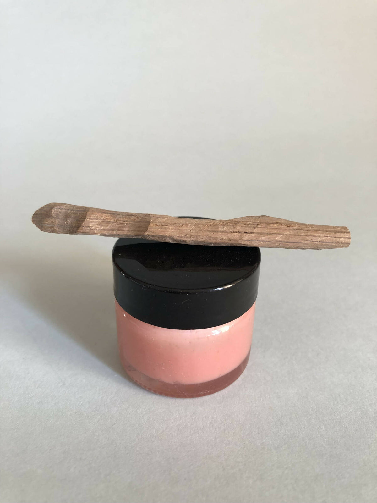 Cuillère à cosmétiques en bois, manche long, posée sur un pot cosmétique.