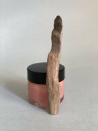 Cuillère à cosmétiques en bois, manche long, posée sur un pot à couvercle noir.