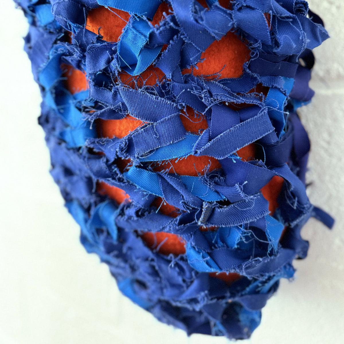 Cocoon décoratif bleu en tissu frangé, avec détails orange visibles
