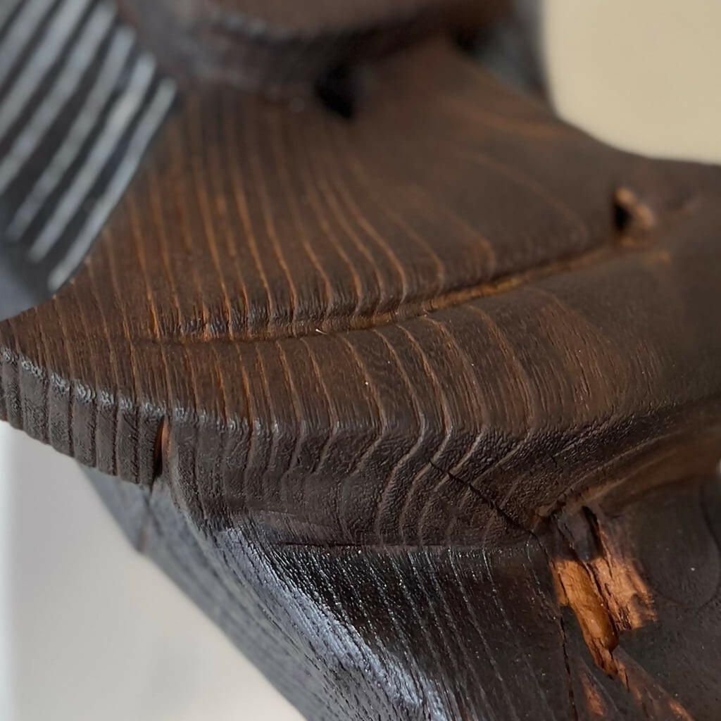 Gros plan : sculpture en bois sombre avec nervures et petites marques