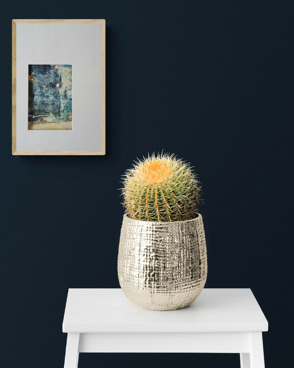 Tableau abstrait en cadre beige, motif bleu-vert, posé au-dessus d’une table blanche.