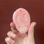 Crâne en céramique rose, visage souriant avec yeux verts et dents blanches