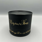 Bougie cylindrique noire « Nez dans les Fleurs » avec inscription dorée.