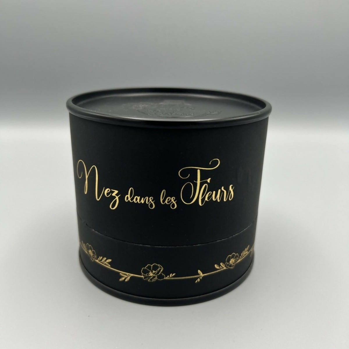 Bougie cylindrique noire « Nez dans les Fleurs » avec inscription dorée.