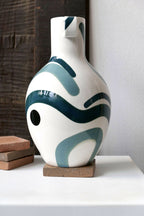 Vase buste en céramique blanche, anses, décor vert/turquoise et formes sombres.