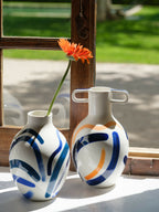 Vases bustes en céramique blanche avec anses, motifs bleu/orange abstraits et une fleur.