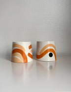 Deux grandes tasses trapèze en céramique blanche, motifs beige et orange.