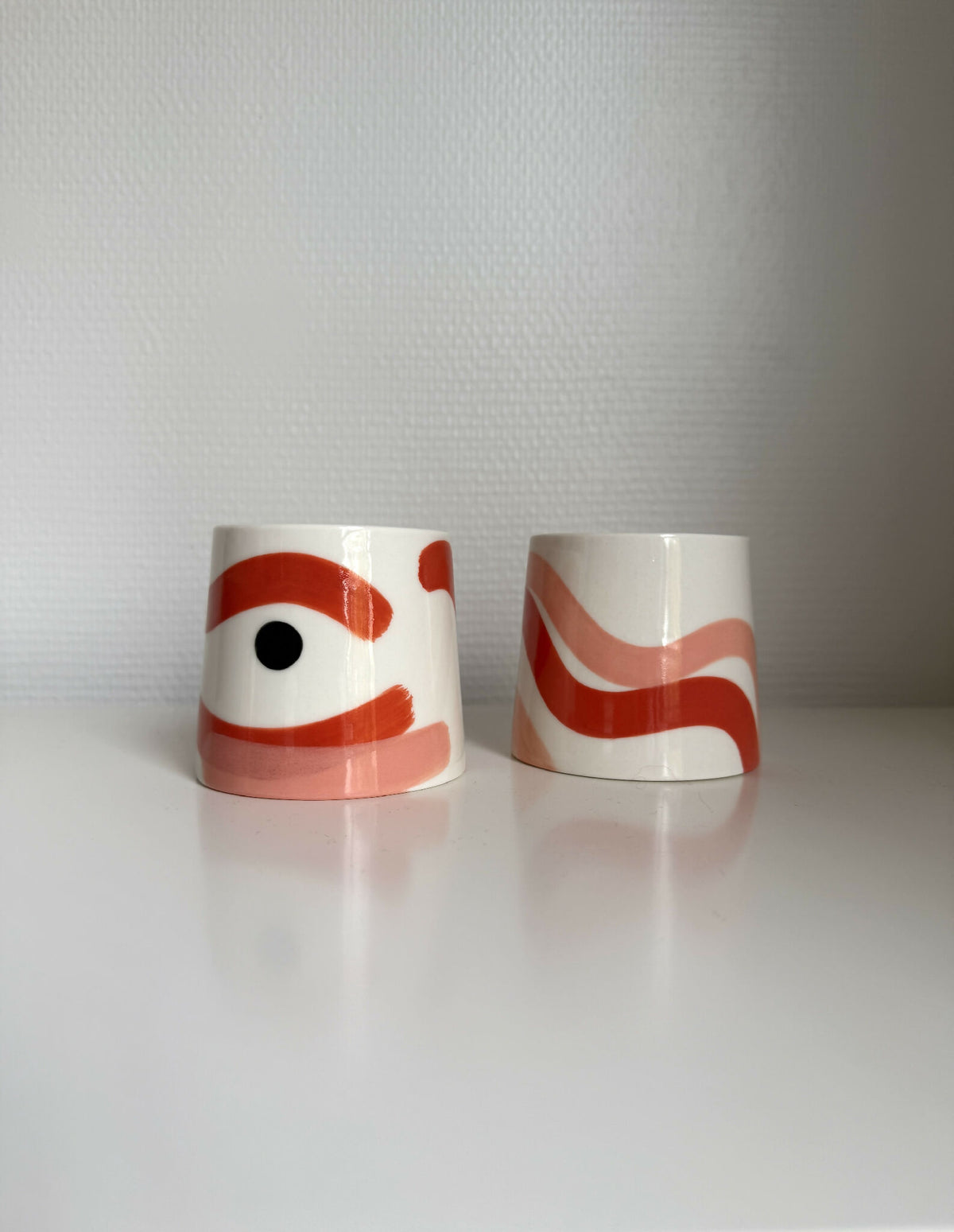 Deux grandes tasses trapèze en céramique blanche, motifs rouge et orange.