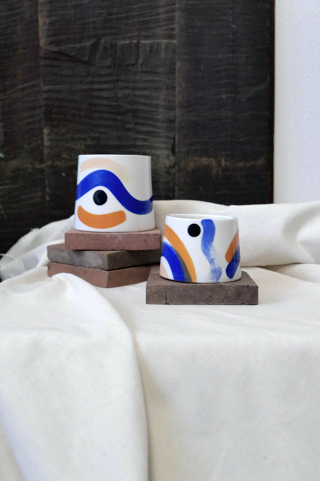 Grande tasse trapèze en céramique blanche, motif bleu et orange, sur socle.
