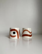 Deux grandes tasses trapèze en céramique blanche, motifs brun et rouge.