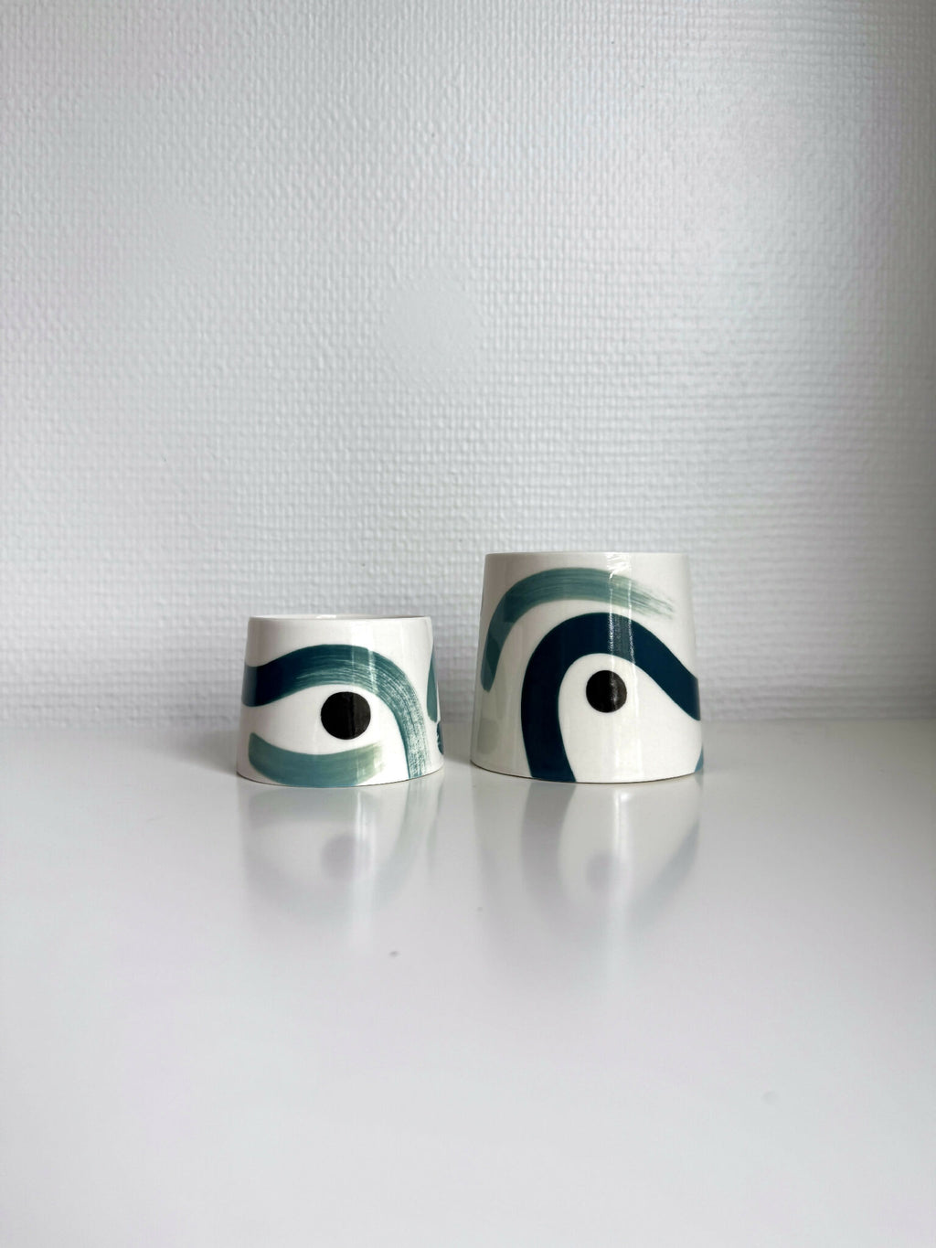 Deux grandes tasses trapèze en céramique blanche, motifs vert et bleu.
