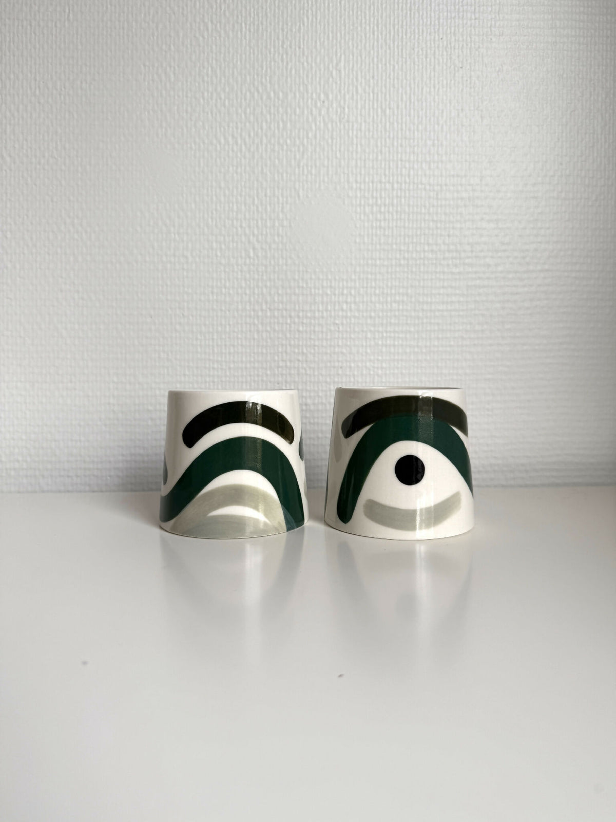 Deux grandes tasses trapèze en céramique blanche, motifs vert foncé et blanc.