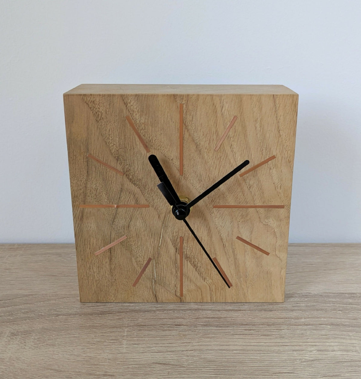 Horloge de bureau carrée en chêne clair, face avant, aiguilles noires et repères colorés.