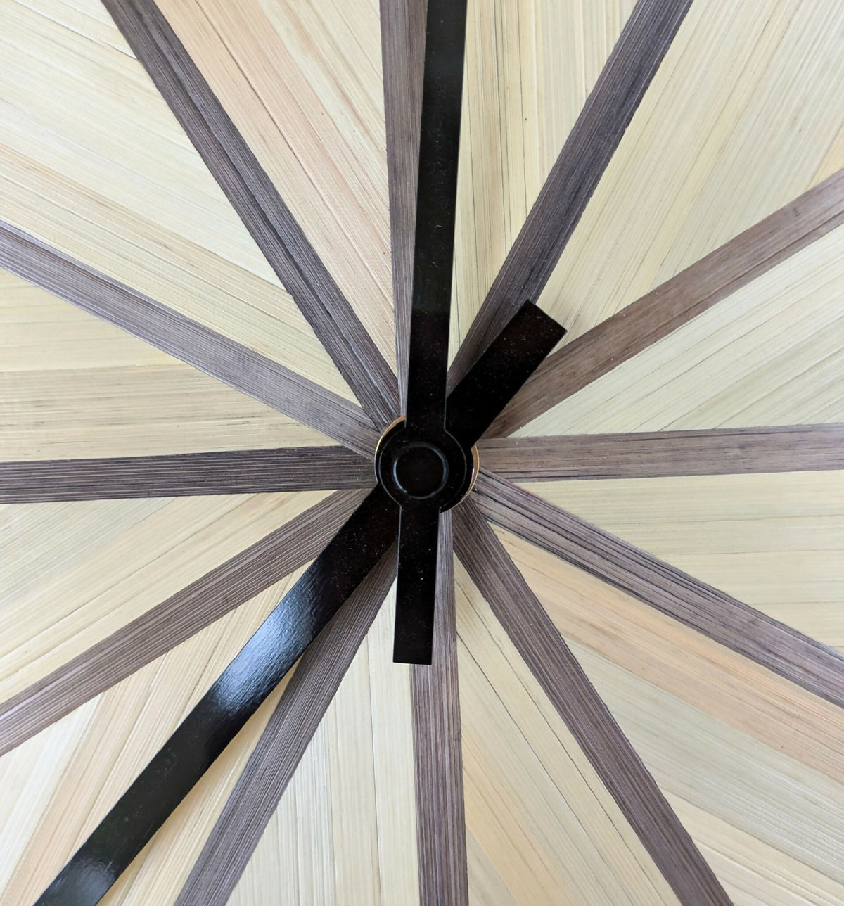 Horloge ronde, gros plan du centre noir et des aiguilles longues en marqueterie