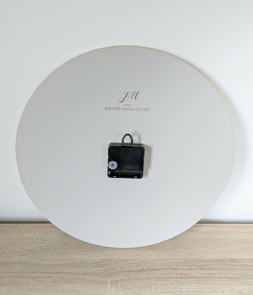 Horloge murale ronde, logo «JM» et mécanisme noir, inscription «Jérôme Marqueterie»