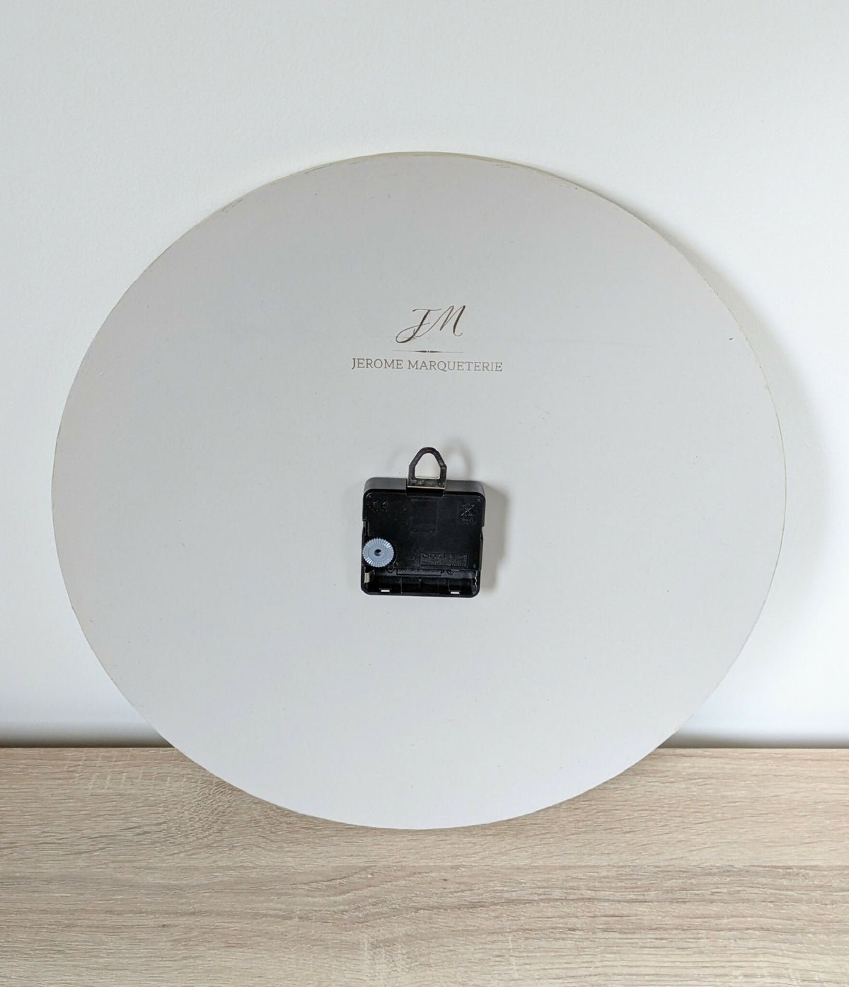 Horloge murale ronde, logo «JM» et mécanisme noir, inscription «Jérôme Marqueterie»