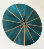 Horloge murale ronde en paille bleu-vert, rayons dorés, centre noir avec aiguilles
