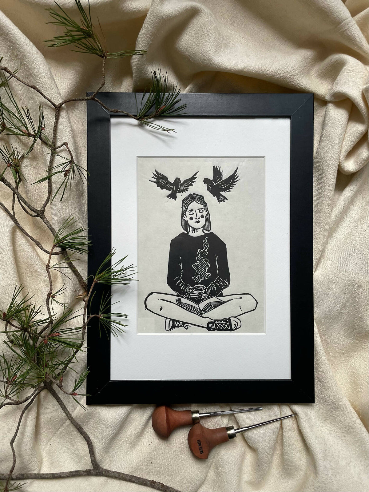 Illustration encadrée noire : femme assise lisant, oiseaux noirs au-dessus, bord blanc.